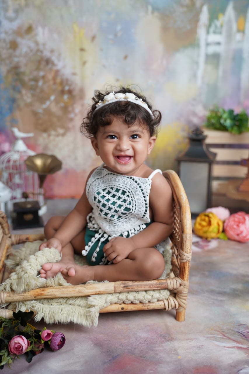 Baby Yanvi laughing on a little rattan bed with flowers around her