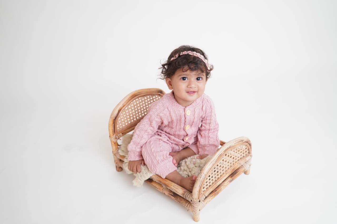 Baby Yanvi in a pink knitted outfit sitting in a rattan bed